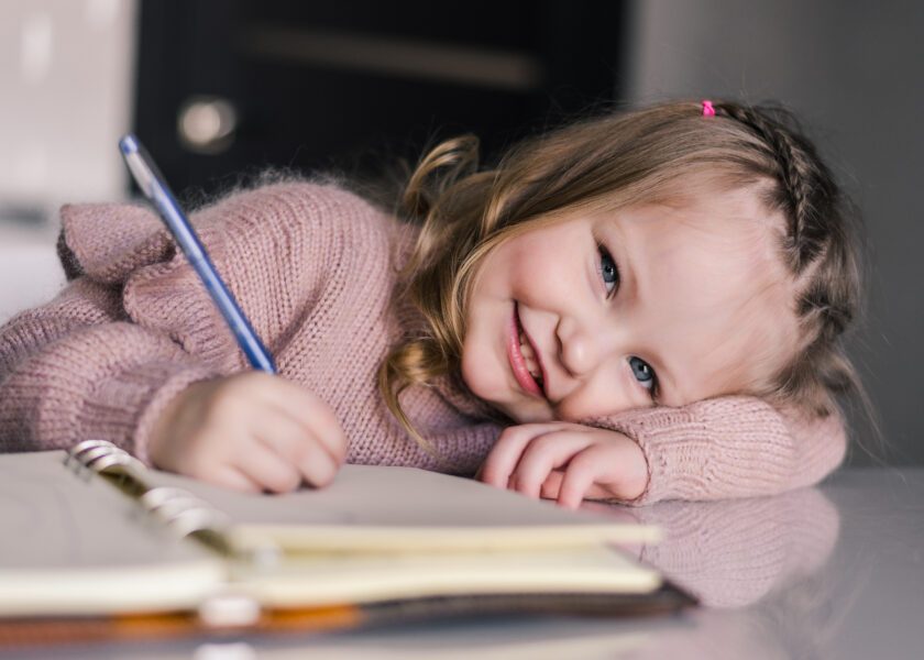 Adorable preschool girl drawing with pen at table. Cute daughter smiling and make kindergarten homework