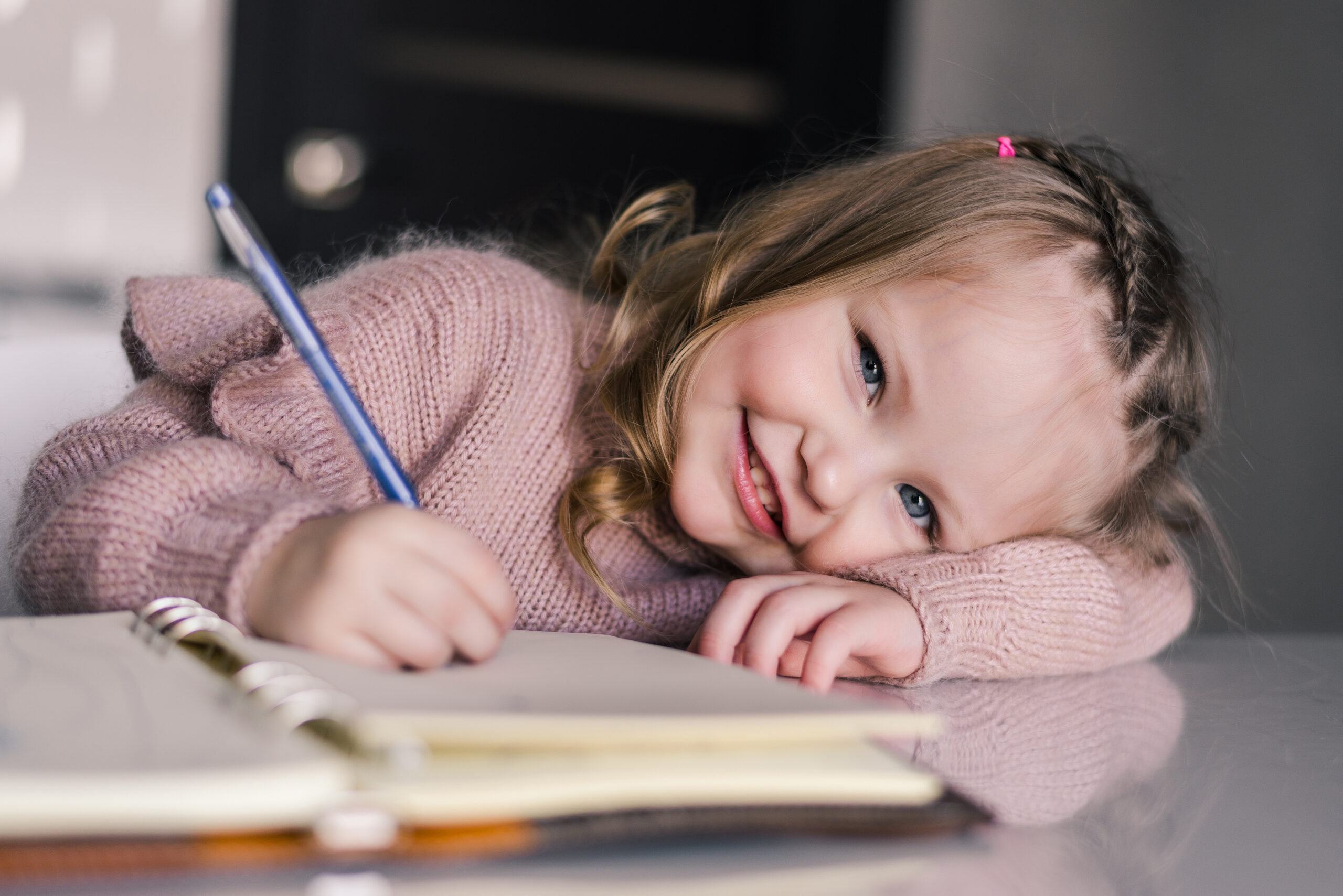 Adorable preschool girl drawing with pen at table. Cute daughter smiling and make kindergarten homework